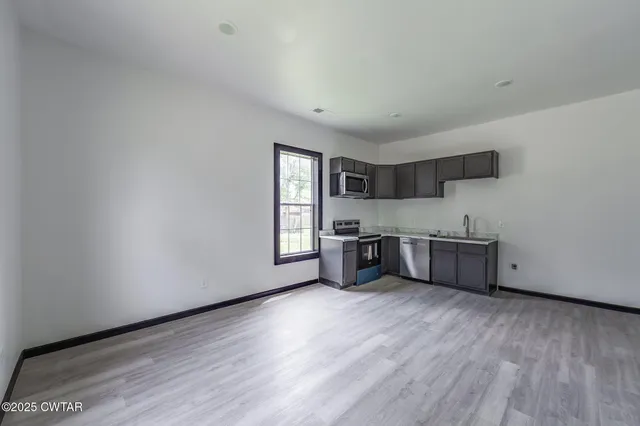 a large white kitchen with stainless steel appliances wooden floors and white walls