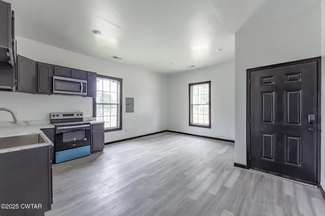 an empty room with wooden floor cabinet and windows