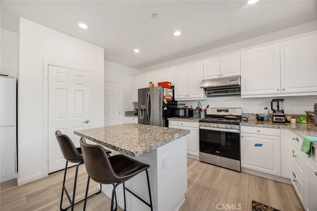 a kitchen with stainless steel appliances granite countertop a stove top oven a sink dishwasher and a refrigerator with wooden floor