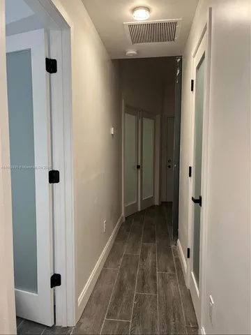 a view of a hallway with wooden floor and a bathroom
