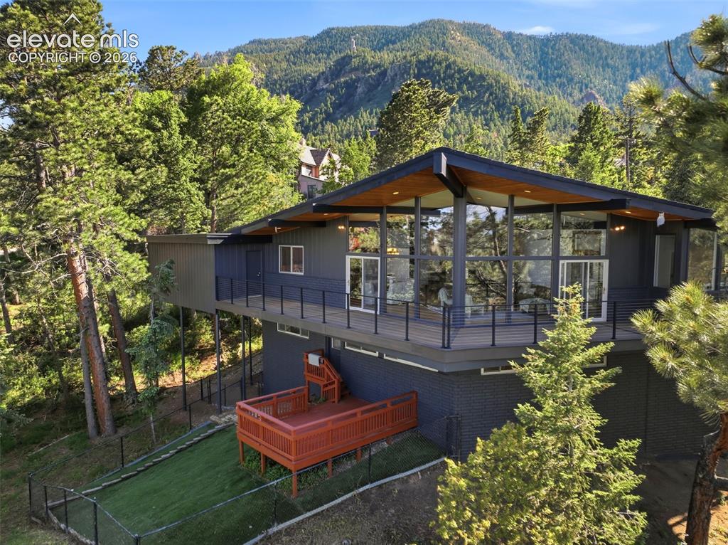 17 Pine Road Colorado Springs, CO 80906 - Photo 47 of 48 Contemporary architectural style residence featuring extensive glazing, a spacious deck with dark railings, a lower-level red-stained wood deck, a fenced turf area, and mature surrounding evergreen trees