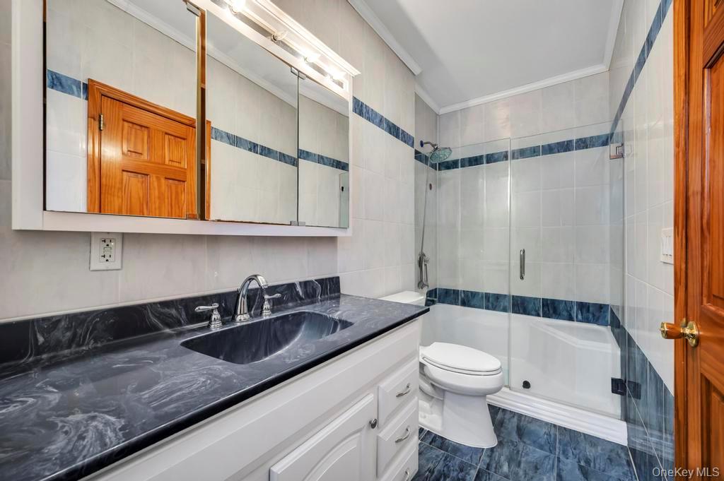 64 Fox Place Hicksville, NY 11801 - Photo 19 of 25 Bathroom featuring tile walls, ornamental molding, a shower stall, and vanity