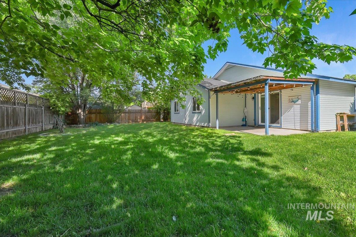 9215 West Preece Street Boise, ID 83704 - Photo 19 of 22 Expansive backyard featuring a lush lawn, privacy fencing, a covered patio with a concrete slab, and a sliding glass door entry to the home