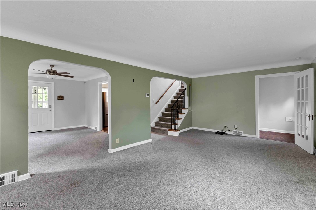 3385 Rosedale Road Cleveland, OH 44112 - Photo 13 of 40 Unfurnished living room featuring carpet floors, arched walkways, baseboards, a ceiling fan, and stairs