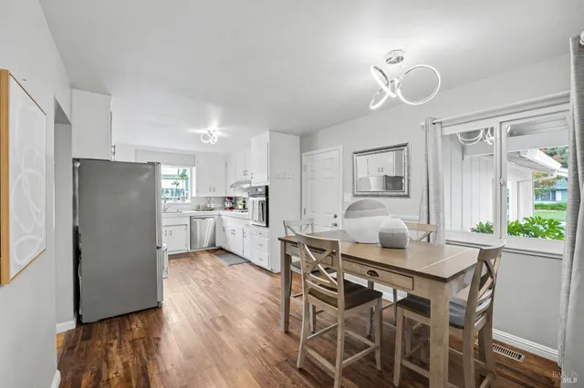 a kitchen with stainless steel appliances kitchen island granite countertop a refrigerator a stove a sink a dining table and chairs with wooden floor