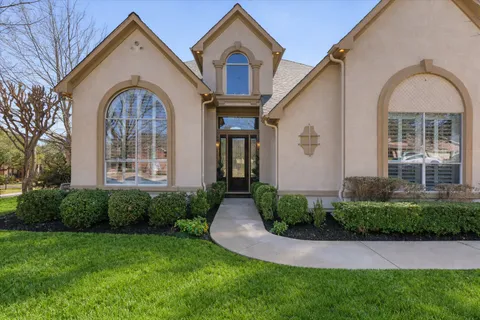 a view of a brick house with a large windows and a yard with plants
