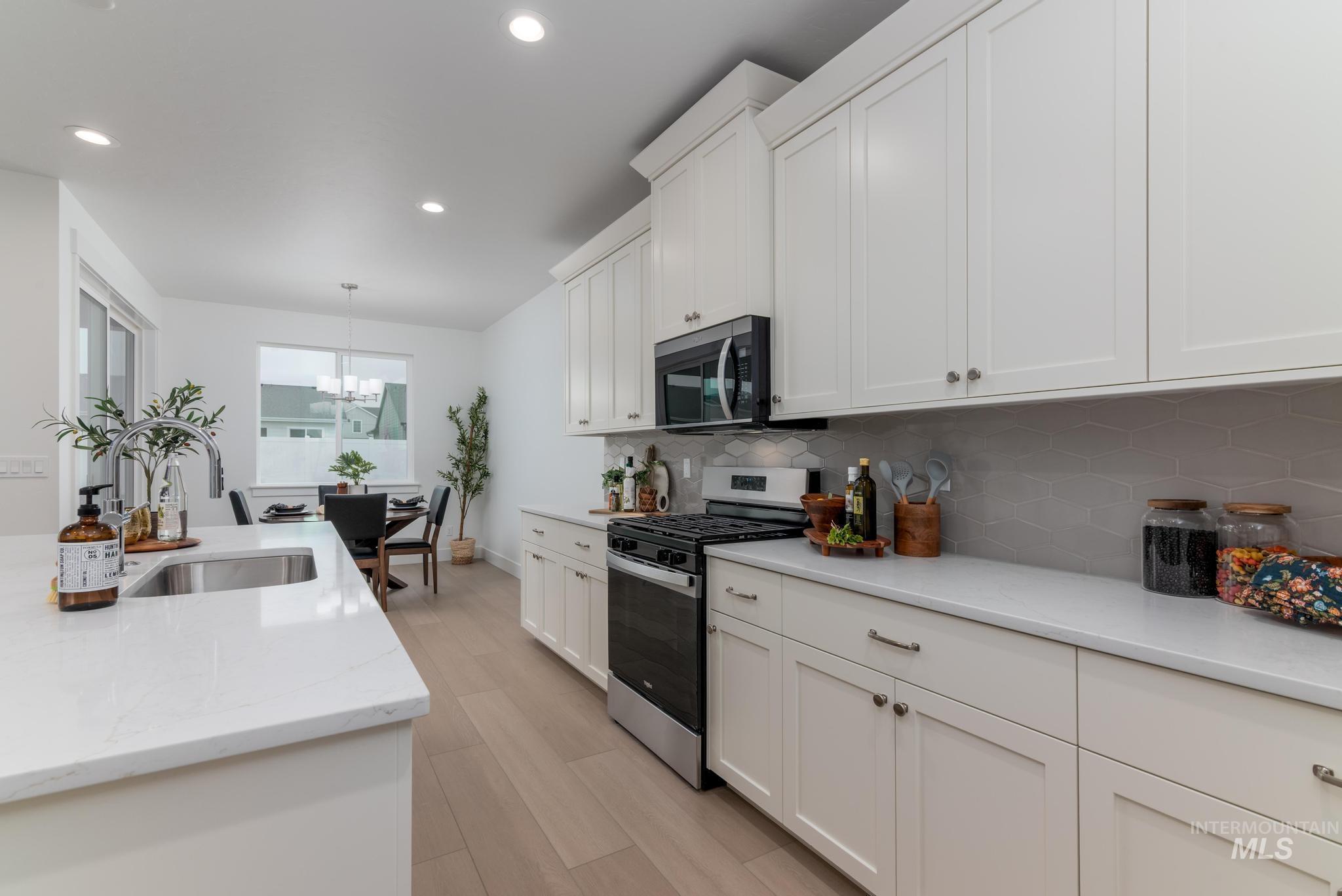 1940 West Chokecherry Avenue Middleton, ID 83644 - Photo 6 of 12 Kitchen featuring stainless steel appliances, white cabinets, light stone counters, light wood-style floors, and hanging lights