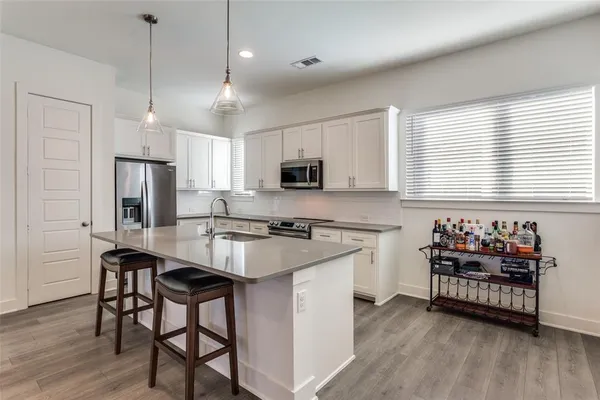 a kitchen with stainless steel appliances granite countertop a stove a sink a microwave a refrigerator and white cabinets with wooden floor