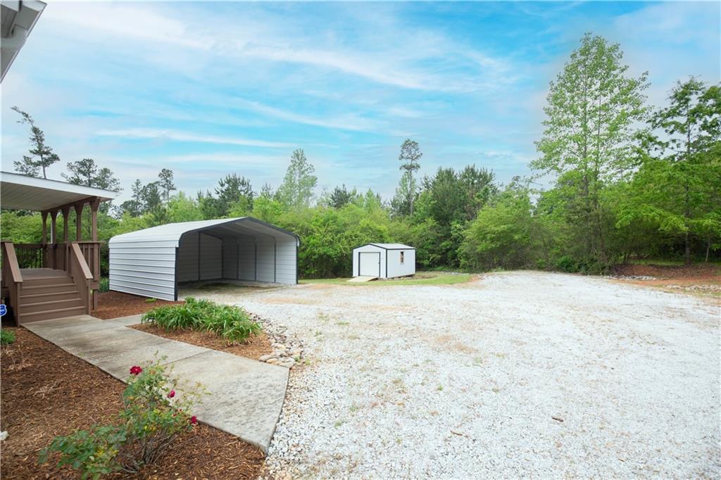 265 A State Rd S-37-141 Westminster, SC 29693 - Photo 4 of 33 A spacious gravel lot features a carport and a storage shed, set against a backdrop of natural woodland.