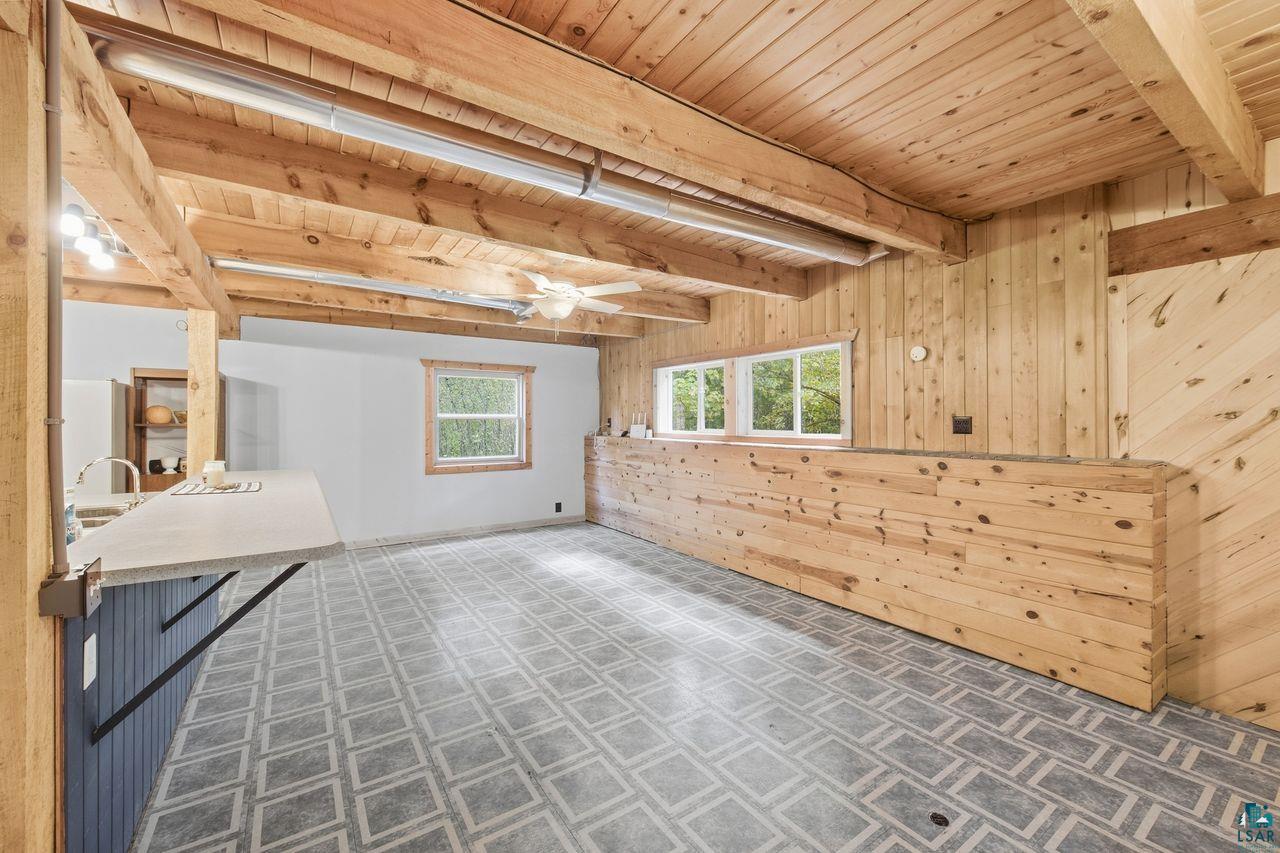 65889 Old County Road Marengo, WI 54855 - Photo 27 of 44 Wood-paneled walls and ceiling with exposed beams, patterned flooring, built-in breakfast bar with a solid surface countertop, and multiple windows providing natural illumination