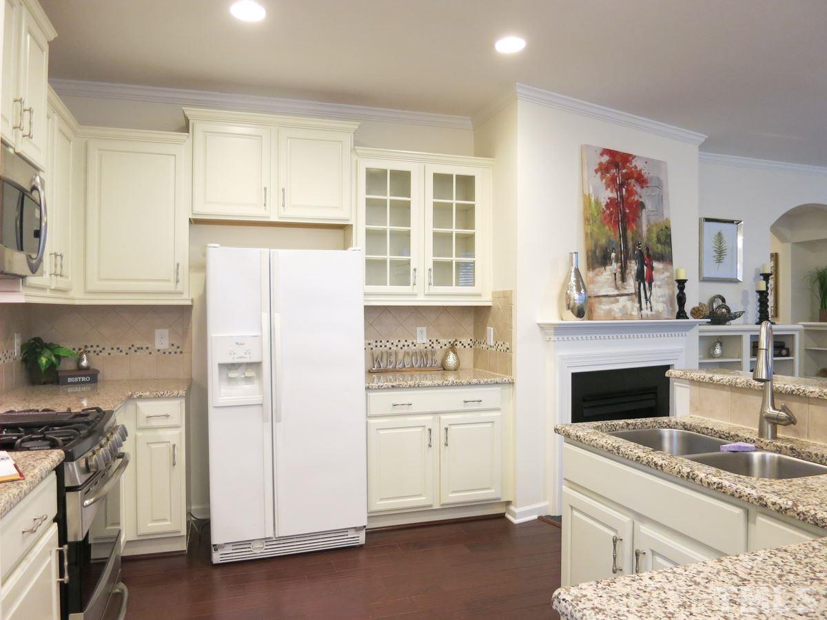 1556 Rodessa Run Raleigh, NC 27607 - Photo 8 of 25 The fabulous Kitchen features granite counters, SS appls (5-burner gas range, MW, DW), lots of cream cabinets (some w/glass doors), tile backsplash, pantry & island w/sink, and it is open to the Living Rm & sunny Dining Area.