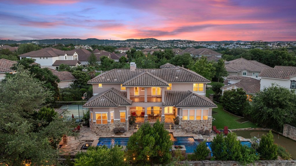 109 Largo Cove Austin, TX 78734 - Photo 4 of 40 Perched on a hill, this impressive multi-story residence boasts a private pool and ample patio space, all beneath a vibrant evening sky.