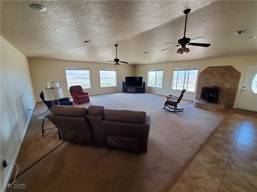 5272 Truman Lane Caliente, NV 89008 - Photo 21 of 39 Living room featuring a textured ceiling, a ceiling fan, a wood stove, baseboards, and carpet