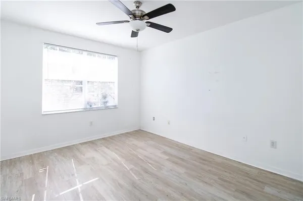 an empty room with wooden floor fan and windows