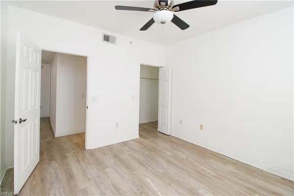 an empty room with wooden floor closet and fan