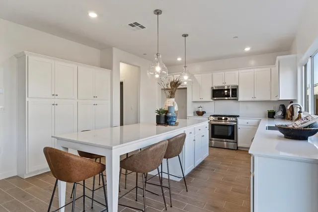 a kitchen with stainless steel appliances a stove a sink a refrigerator and white cabinets with wooden floor