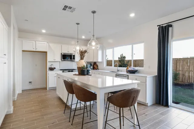 a kitchen with stainless steel appliances kitchen island granite countertop a dining table chairs and white cabinets