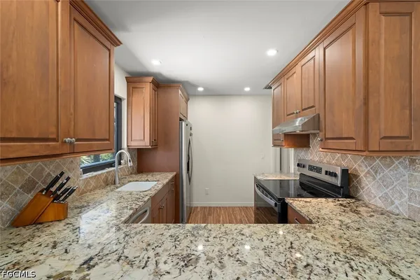 a kitchen with stainless steel appliances granite countertop a refrigerator a stove and a sink with wooden cabinets
