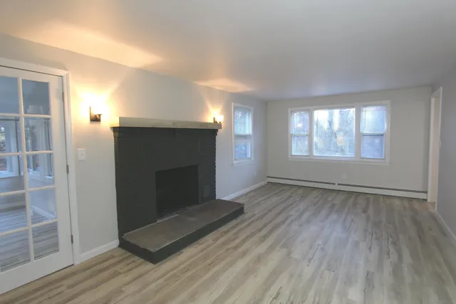 an empty room with wooden floor fireplace and windows