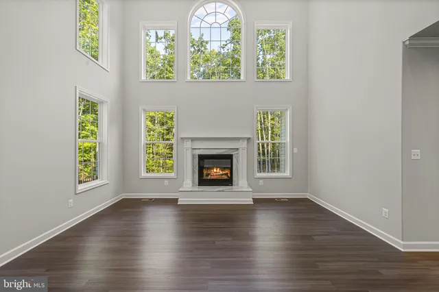 a view of an empty room with wooden floor a fireplace and a window