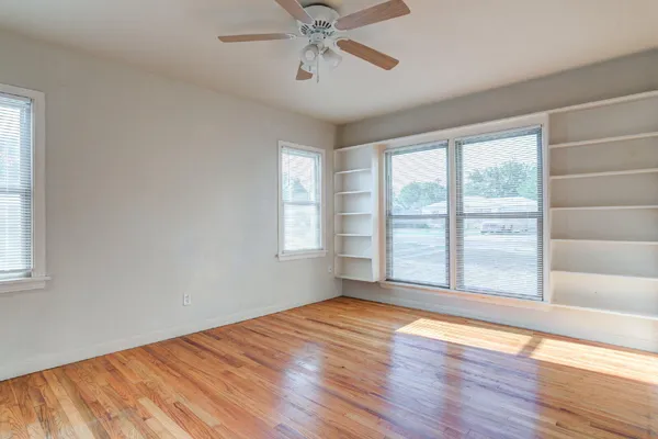 an empty room with wooden floor fan and windows
