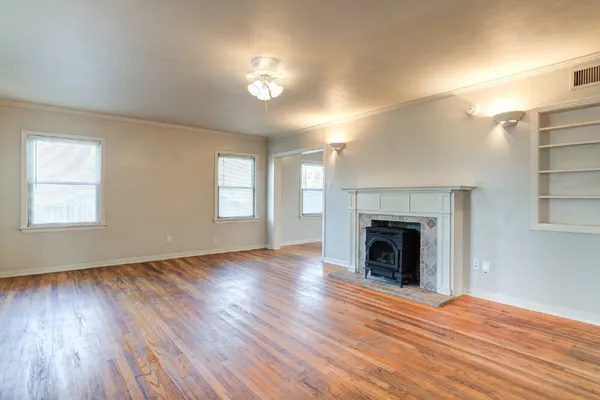 an empty room with wooden floor fireplace and windows
