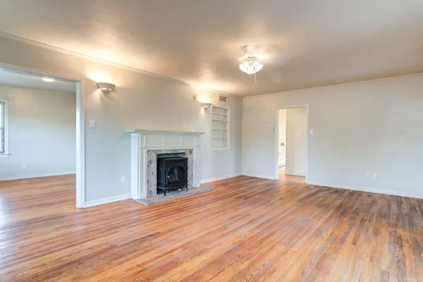 a view of an empty room with wooden floor fireplace and a window