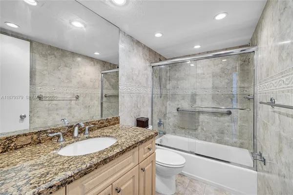 a bathroom with a granite countertop sink a toilet a mirror and shower