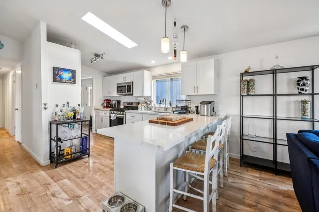 a kitchen with stainless steel appliances granite countertop a refrigerator a sink dishwasher a stove and white cabinets with wooden floor