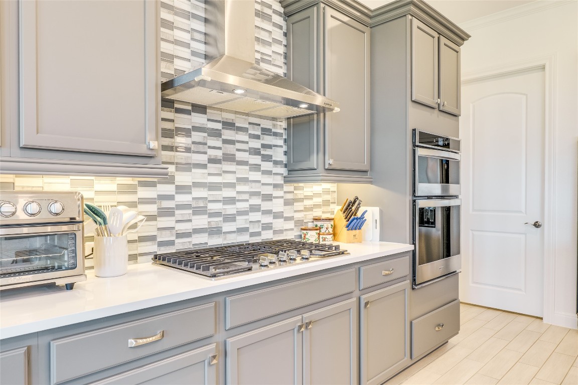 616 Climbing Rock Loop Dripping Springs, TX 78620 - Photo 6 of 35 Kitchen with backsplash, wall chimney range hood, gray cabinets, stainless steel appliances, and crown molding