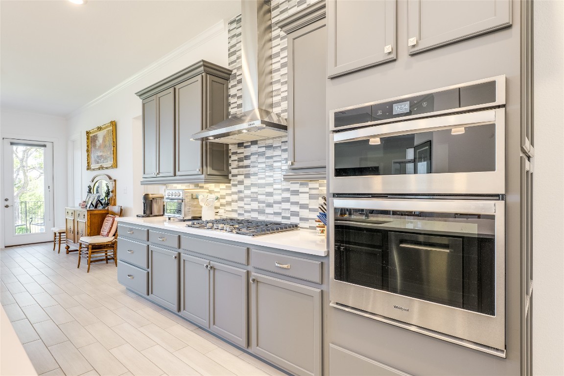 616 Climbing Rock Loop Dripping Springs, TX 78620 - Photo 7 of 35 Kitchen with appliances with stainless steel finishes, ornamental molding, backsplash, wall chimney exhaust hood, and gray cabinets