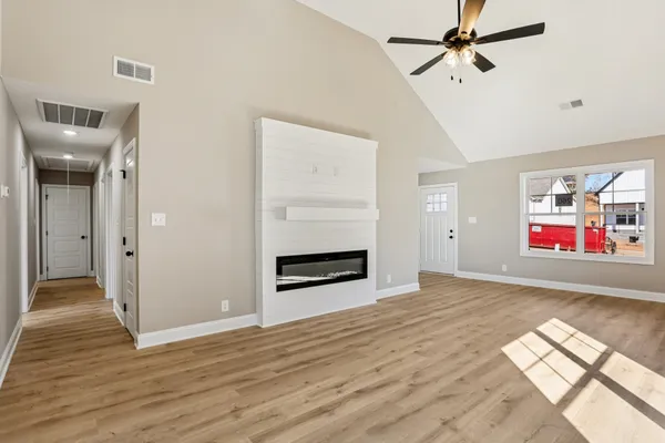 an empty room with wooden floor chandelier fan and windows