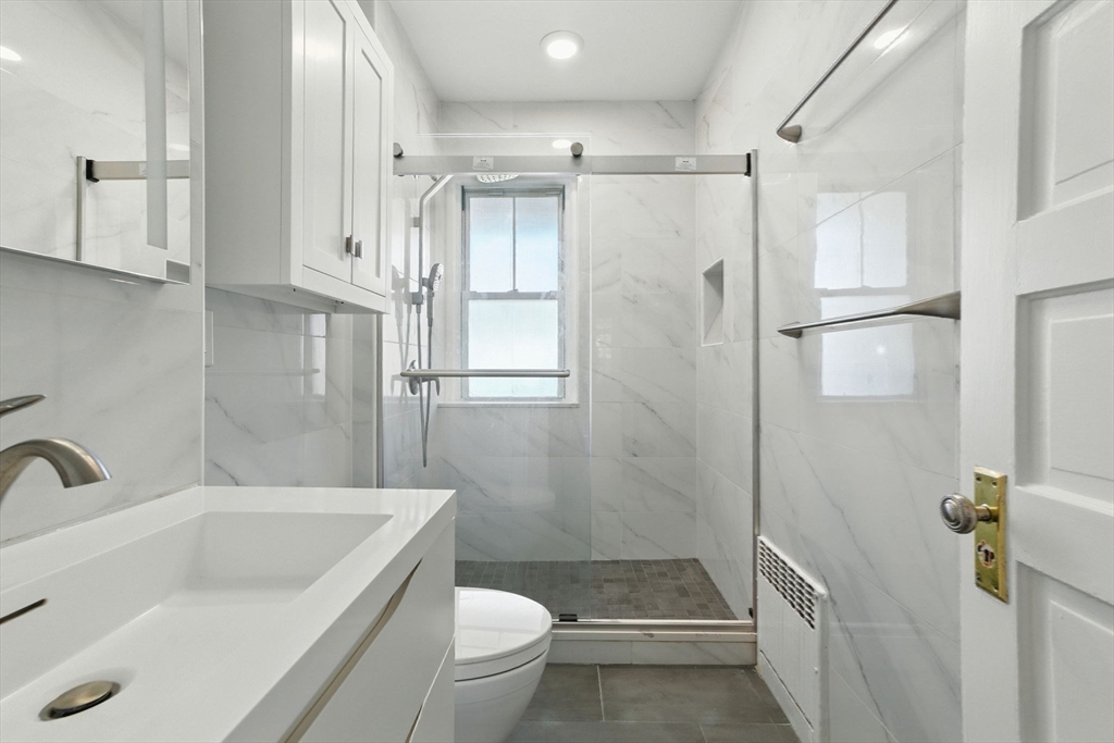 17 Strathmore Road, Unit 2 Brookline, MA 02445 - Photo 29 of 32 a bathroom with a granite countertop bathtub shower sink vanity and toilet