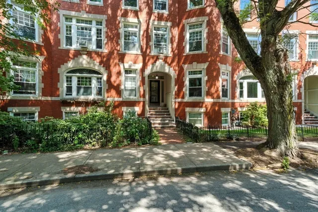 a view of a brick building next to a road with plants and trees
