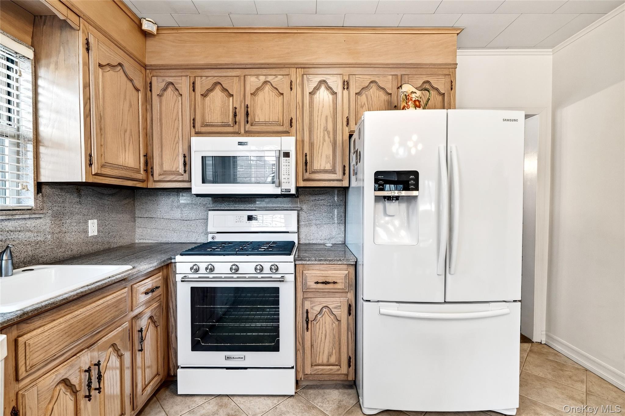 3334 Country Club Road Bronx, NY 10465 - Photo 19 of 49 Kitchen with white appliances, backsplash, light tile patterned flooring, dark stone counters, and brown cabinets