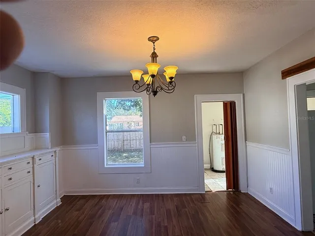 a dining room with wooden floor a chandelier a flat screen tv and a window