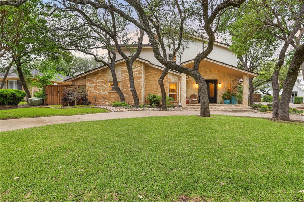 8877 Random Road Fort Worth, TX 76179 - Photo 1 of 40 Two-story exterior featuring stone and brick facade, a covered front porch, mature trees, a manicured lawn, and a curved paved driveway