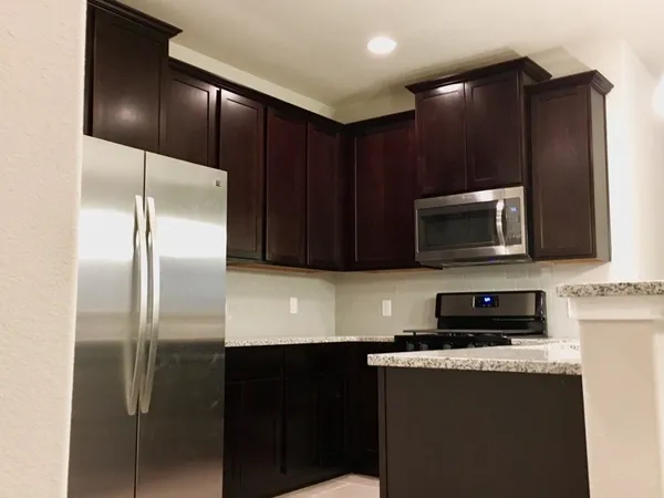 a kitchen with granite countertop a refrigerator a microwave a sink and cabinets