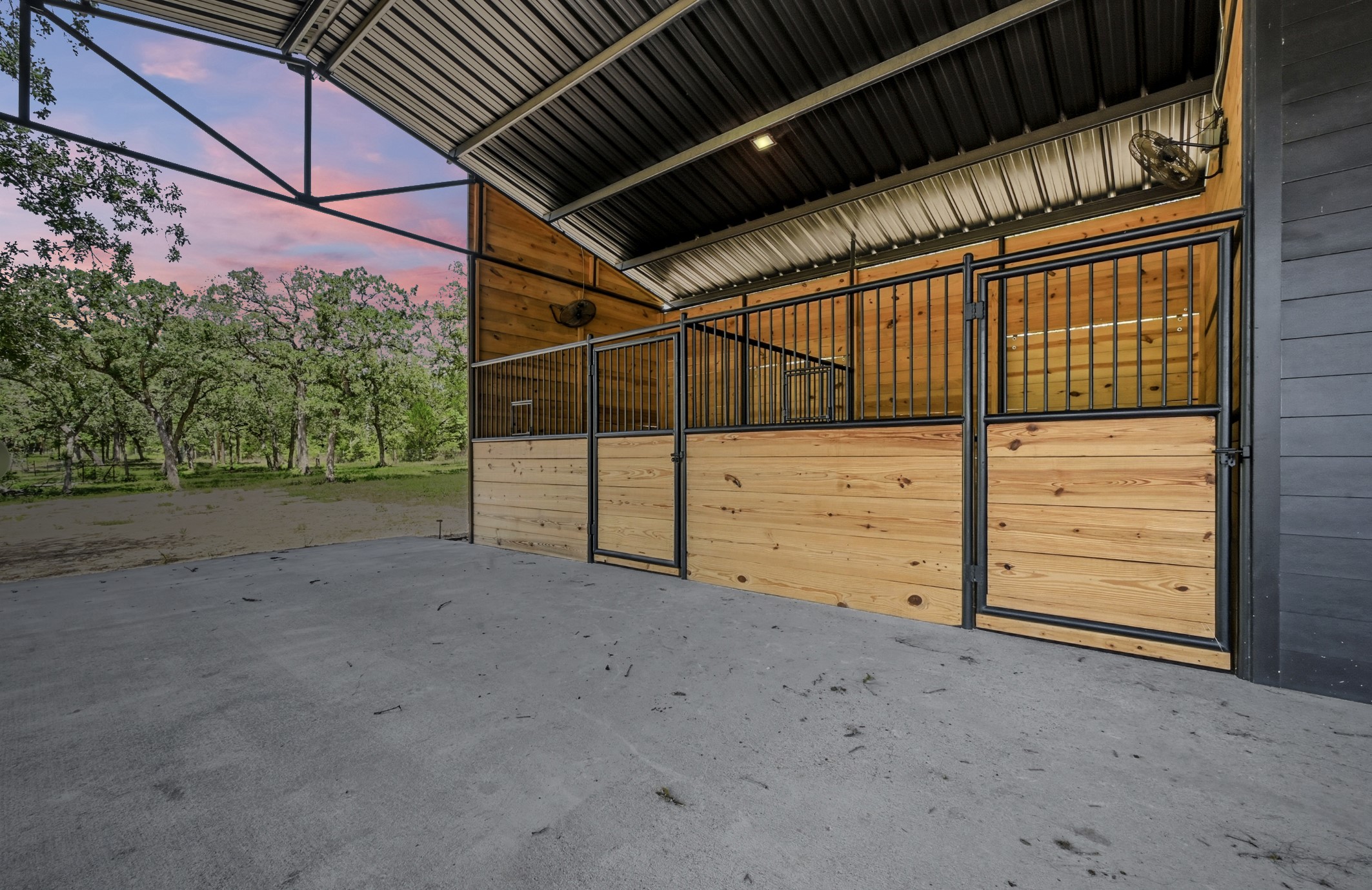 387 Corral Road Smithville, TX 78957 - Photo 35 of 40 Barn interior featuring wood-paneled stalls with black metal grates and doors, a corrugated metal roof, and concrete flooring