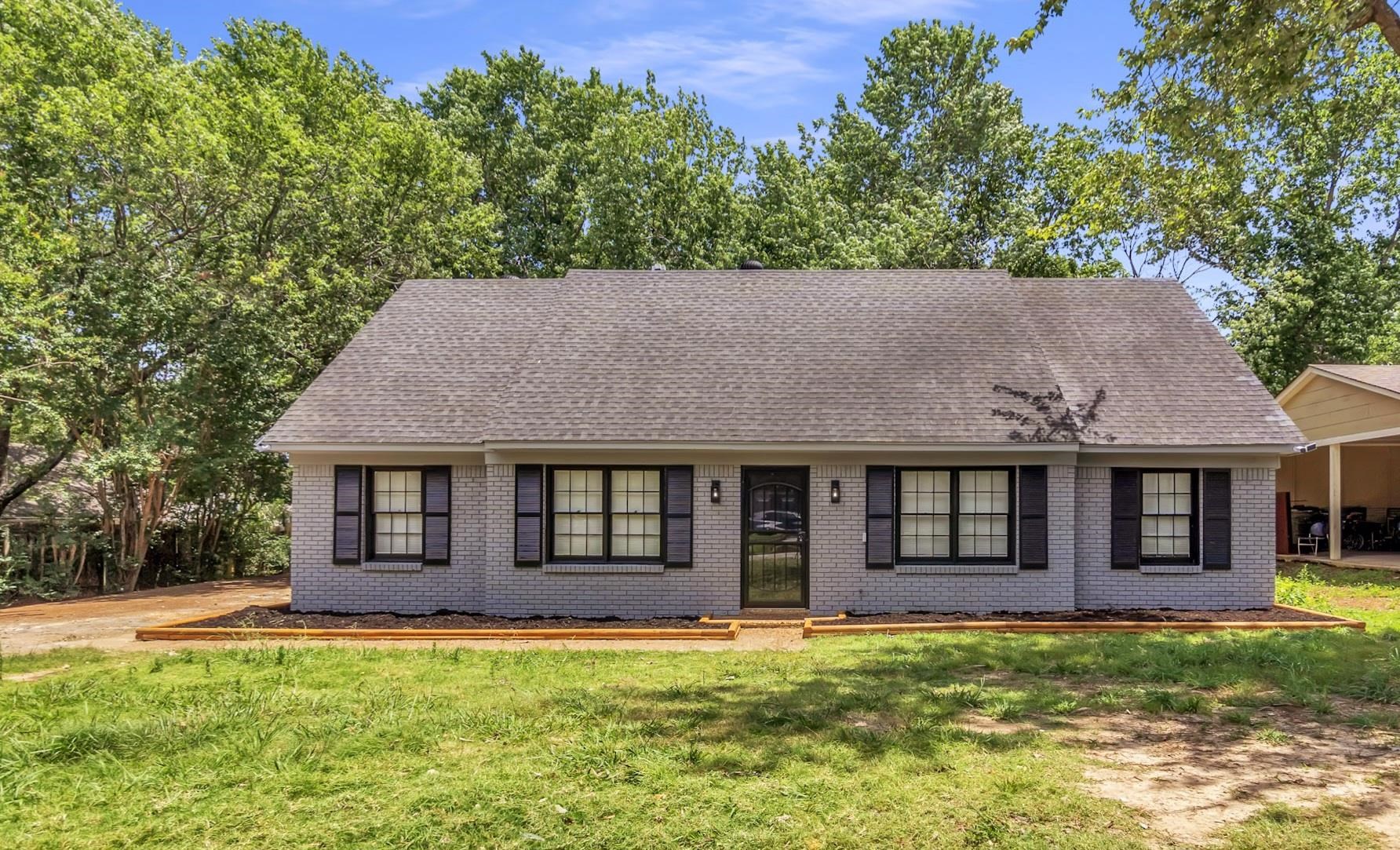 Single-story residential property featuring a light grey brick exterior, black window shutters, and a dark grey shingled roof