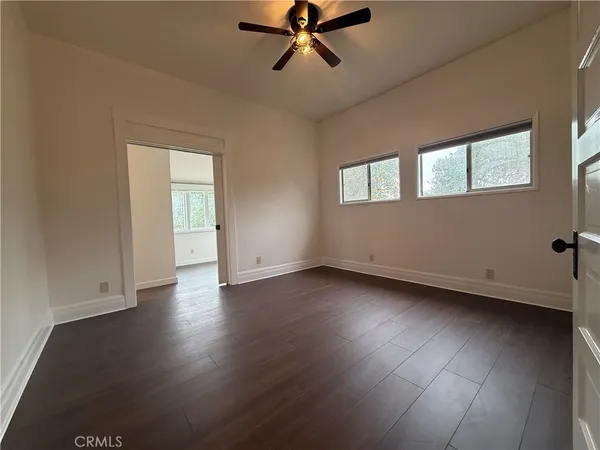 an empty room with wooden floor fan and windows