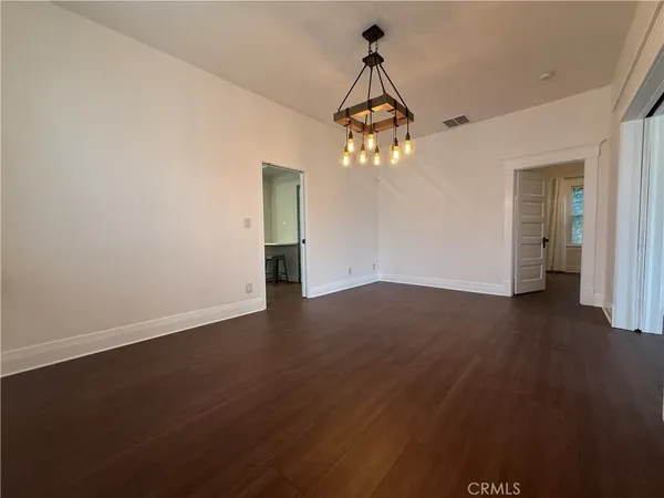 an empty room with wooden floor chandelier and windows