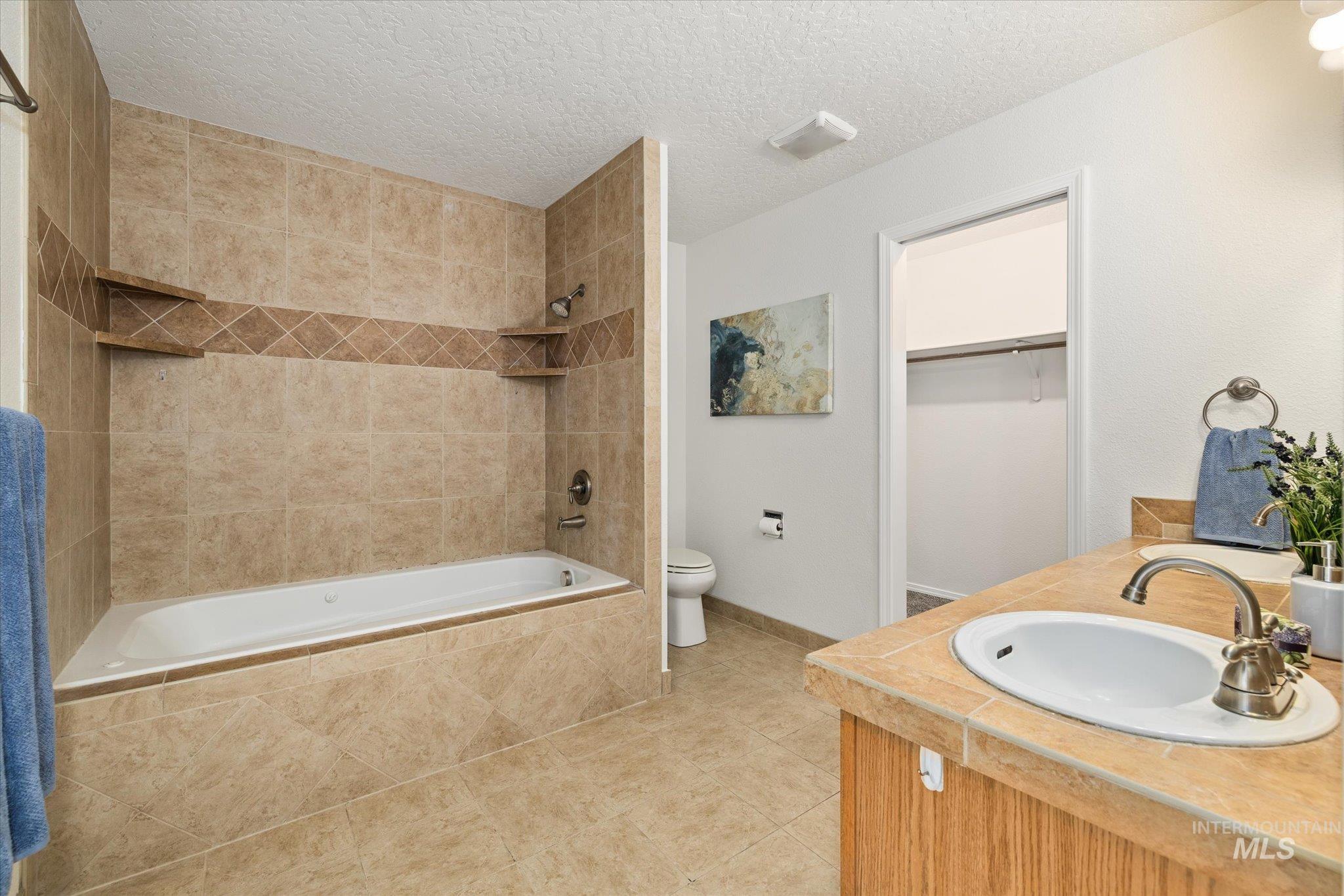 1399 West Gander Drive Meridian, ID 83642 - Photo 24 of 40 Bathroom with tiled shower / bath combo, a walk in closet, double vanity, a textured ceiling, and light tile patterned flooring