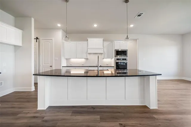 a kitchen with granite countertop a white cabinets and wooden floor