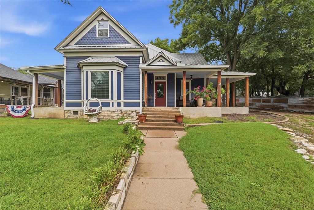 415 South Rice Street Hamilton, TX 76531 - Photo 1 of 28 Blue siding exterior featuring a prominent bay window with white trim, a covered front porch with wood columns, and a red entry door