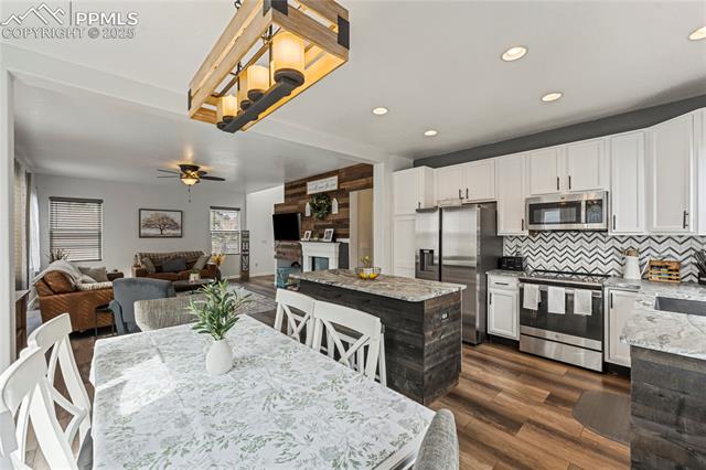 10158 Angeles Road Peyton, CO 80831 - Photo 9 of 43 Kitchen featuring white cabinets, dark wood-type flooring, decorative backsplash, stainless steel appliances, and ceiling fan with notable chandelier