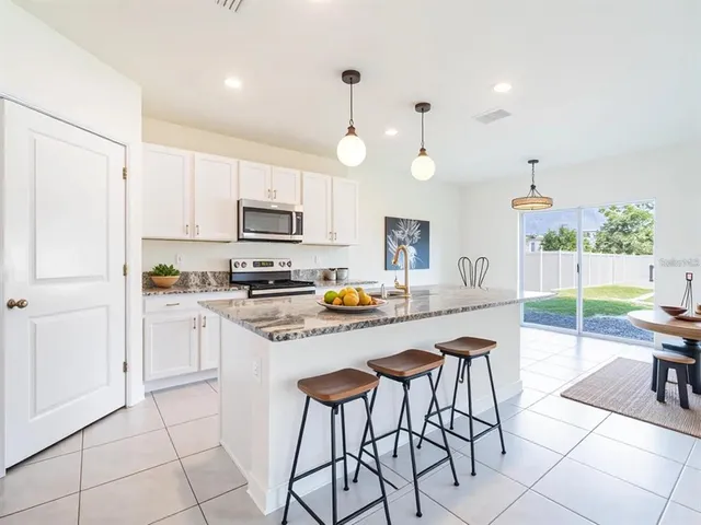 a kitchen with stainless steel appliances kitchen island granite countertop a refrigerator a stove a dining table and chairs with wooden floor