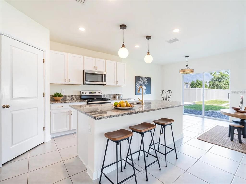 5510 Oxford Gray Road Wesley Chapel, FL 33545 - Photo 9 of 41 a kitchen with stainless steel appliances kitchen island granite countertop a refrigerator a stove a dining table and chairs with wooden floor