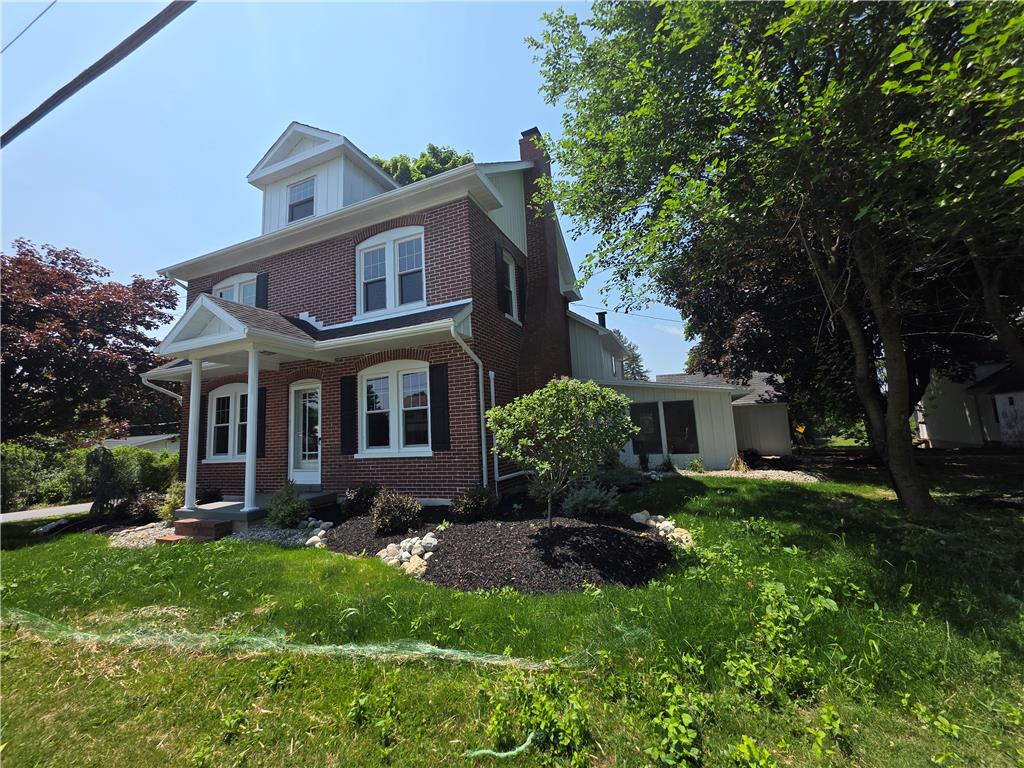 A classic brick facade welcomes with a charming covered front porch, amidst lush landscaping.