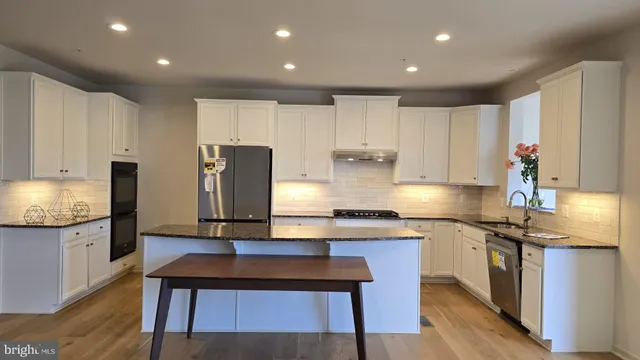 a large kitchen with stainless steel appliances granite countertop a stove a sink a refrigerator and white cabinets with wooden floor